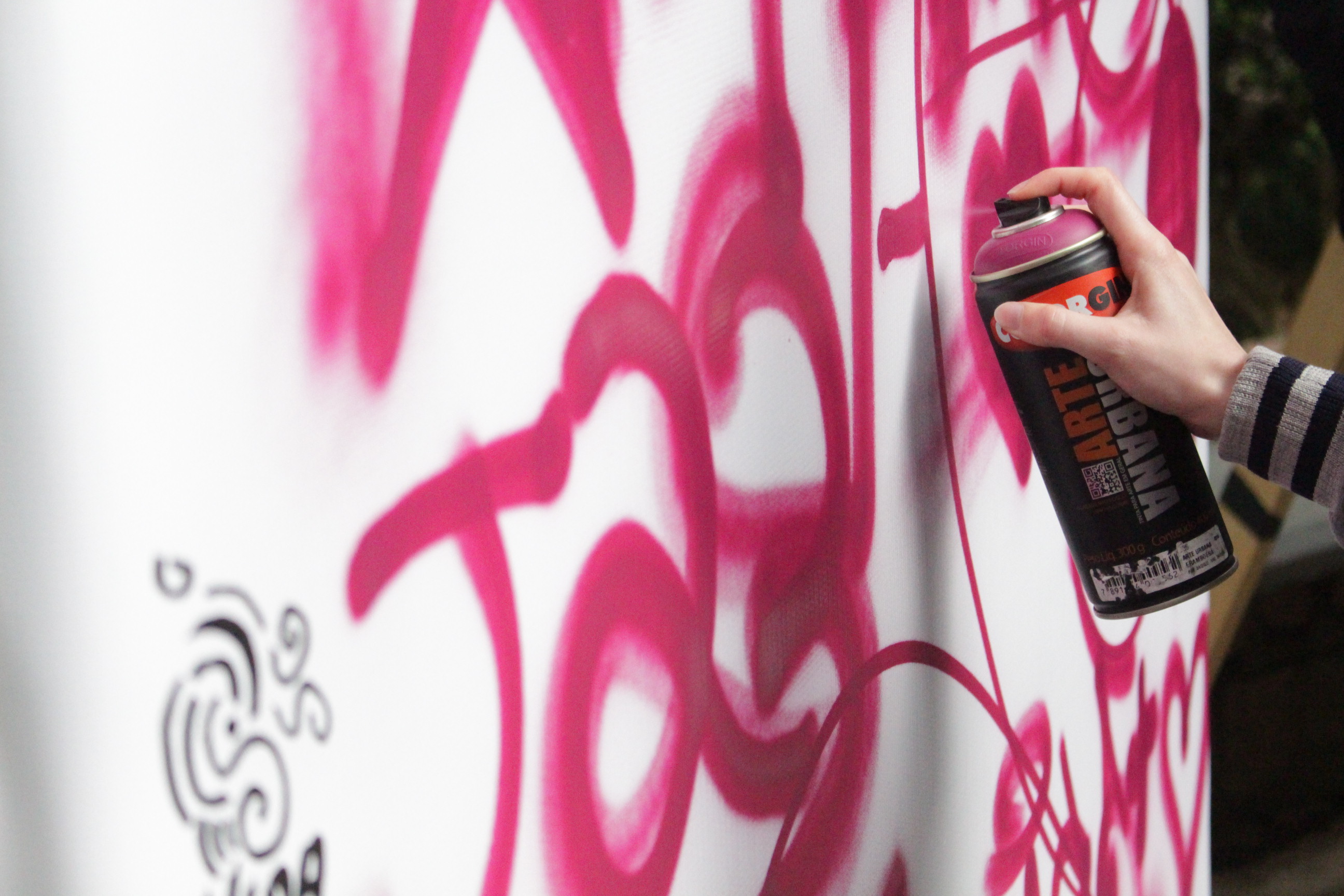 Pessoa segurando uma lata de spray enquanto pinta um mural branco